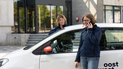 Op dit beeld is te zien hoe Jessica Stok bij een auto van Oost West Wonen staat te bellen met haar collega op de achtergrond.